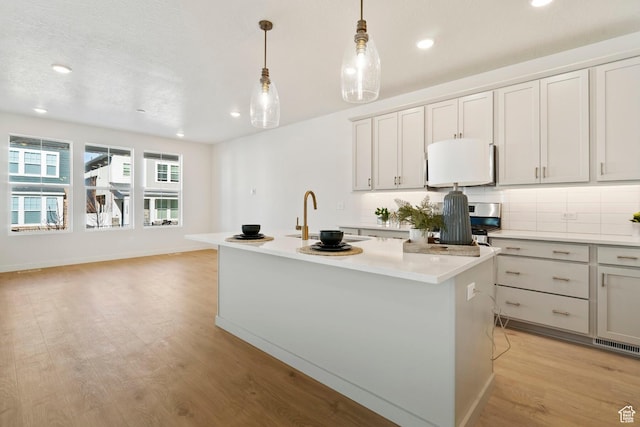 10033 N Torreya Dr Unit 737, Highland, UT 84003 - kitchen featuring a sink, light countertops, a center island with sink, hanging light fixtures, and light wood-style floors