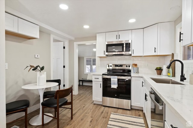 kitchen with stainless steel appliances, a sink, decorative backsplash, light wood-style flooring, and recessed lighting