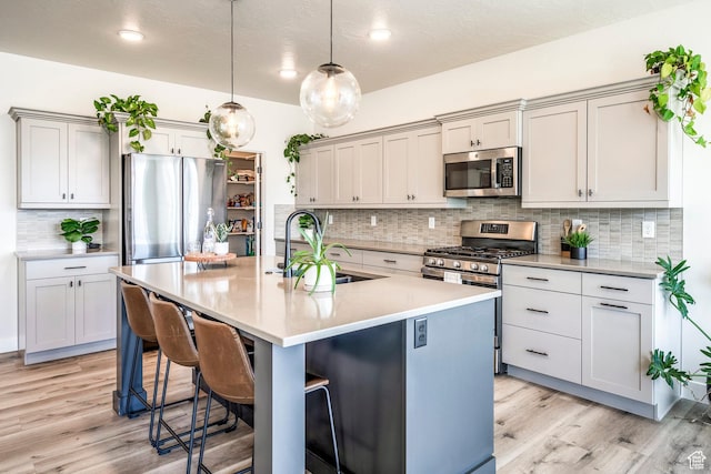 581 W Cypress Umber Dr Unit 34, St George, UT 84790 - kitchen with appliances with stainless steel finishes, a breakfast bar, light wood-style floors, backsplash, and an island with sink