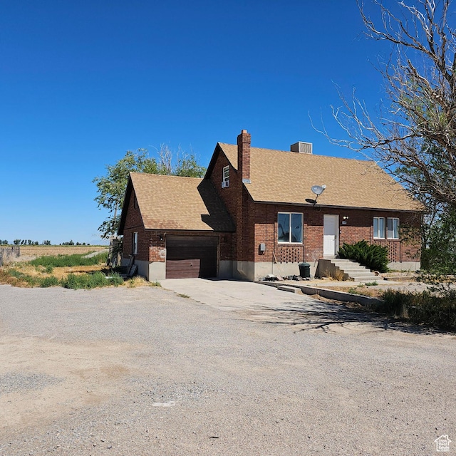 view of front facade with roof with shingles, concrete driveway, a garage, brick siding, and a chimney