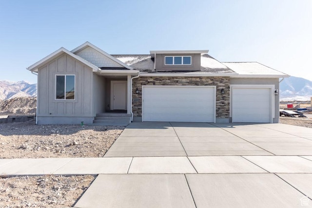 view of front of property with concrete driveway, an attached garage, board and batten siding, a mountain view, and stone siding