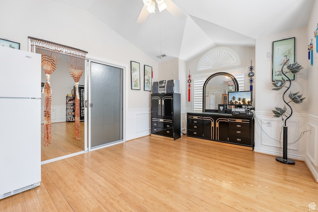 interior space featuring a decorative wall, a ceiling fan, a wainscoted wall, light wood-style flooring, and lofted ceiling