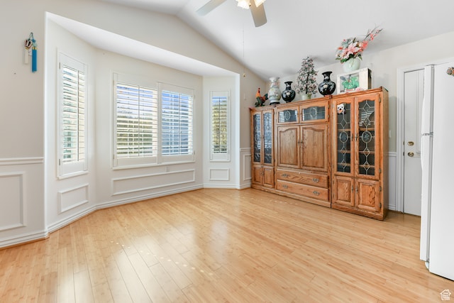 dining room with light wood-style flooring, vaulted ceiling, a ceiling fan, and a wainscoted wall