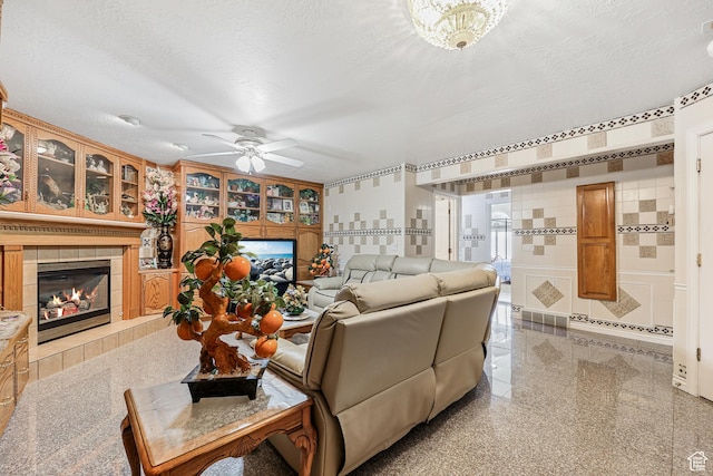 living area with a tile fireplace, a textured ceiling, a ceiling fan, and granite finish floor