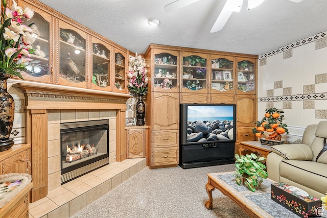 living room with a textured ceiling, light colored carpet, a tiled fireplace, and a ceiling fan
