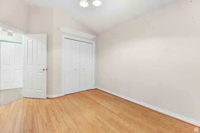 unfurnished bedroom with a closet, wood finished floors, baseboards, and vaulted ceiling
