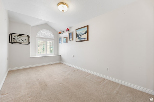 spare room featuring light colored carpet, baseboards, and vaulted ceiling