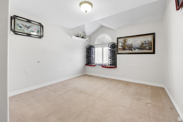 carpeted empty room featuring baseboards and vaulted ceiling