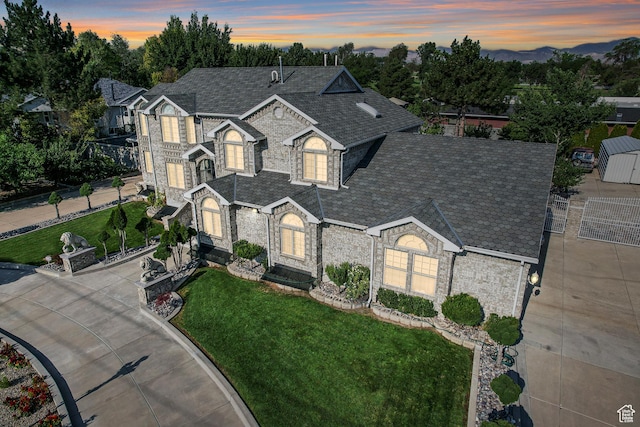 traditional-style home featuring driveway, stone siding, a yard, fence, and a shingled roof