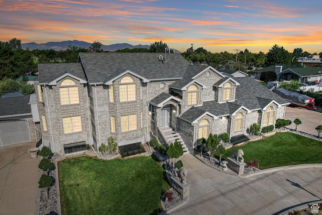 traditional-style home featuring concrete driveway, roof with shingles, a mountain view, stone siding, and a front yard