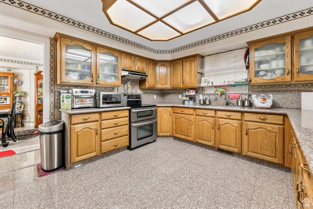 kitchen featuring a sink, appliances with stainless steel finishes, granite finish floor, under cabinet range hood, and decorative backsplash