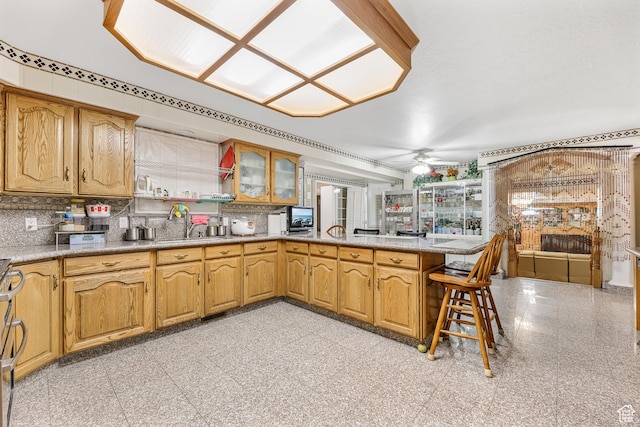 kitchen with tasteful backsplash, glass insert cabinets, a sink, ceiling fan, and a peninsula