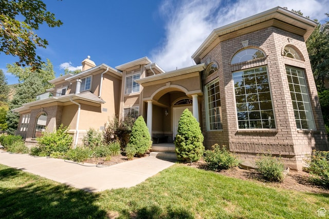 view of front of home featuring stucco siding, brick siding, and a chimney