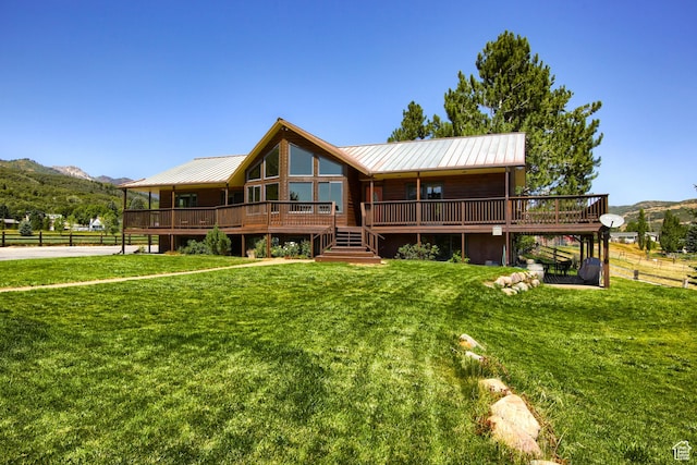 rear view of house with a standing seam roof, fence, a deck with mountain view, metal roof, and a lawn