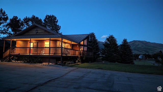 back of house at dusk featuring metal roof, a standing seam roof, a lawn, a mountain view, and a porch