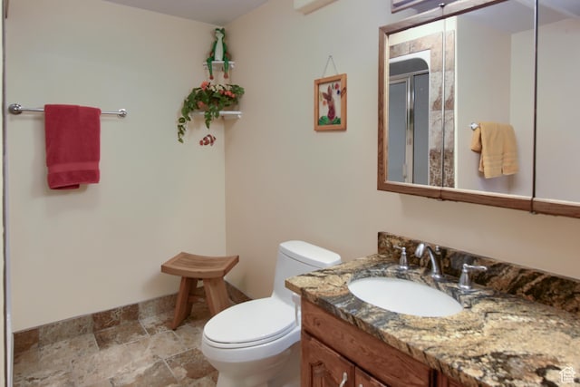 bathroom with vanity, toilet, baseboards, a shower stall, and stone finish flooring