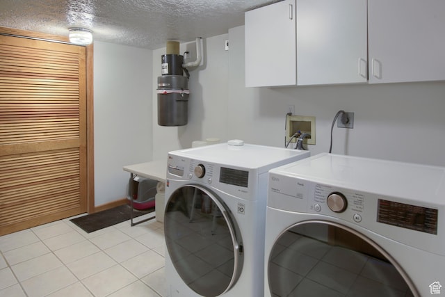 clothes washing area with washing machine and clothes dryer, cabinet space, a textured ceiling, and light tile patterned floors