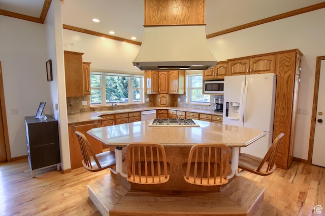 kitchen with light wood finished floors, island range hood, tasteful backsplash, and white appliances