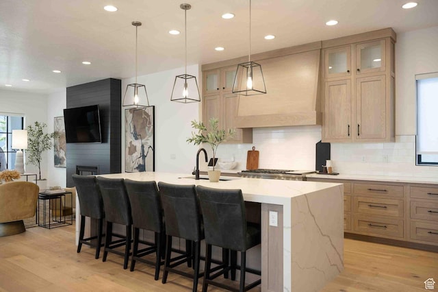 5346 Cyan Ln, St George, UT 84790 - kitchen featuring light wood finished floors, light stone countertops, tasteful backsplash, an island with sink, and custom range hood