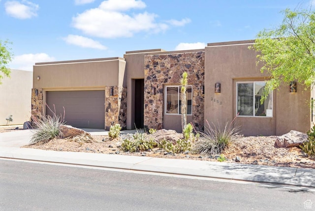 pueblo revival-style home featuring stone siding, driveway, an attached garage, and stucco siding