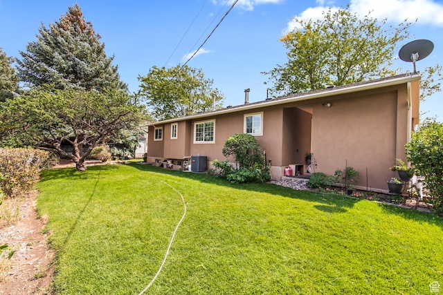 rear view of house featuring stucco siding, a yard, and central AC