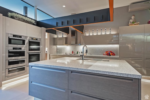 kitchen with a warming drawer, tasteful backsplash, a wall unit AC, and gray cabinets