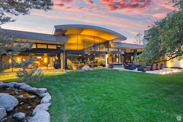 back of house at dusk with outdoor lounge area, a lawn, and a patio