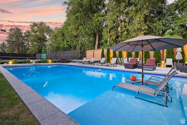 pool at dusk featuring a patio, fence, and a fenced in pool