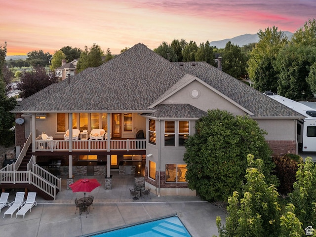 back of house at dusk featuring an outdoor pool, stucco siding, stairs, and a patio area