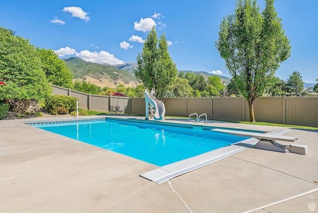 view of pool featuring a diving board, a water slide, a mountain view, and a patio area