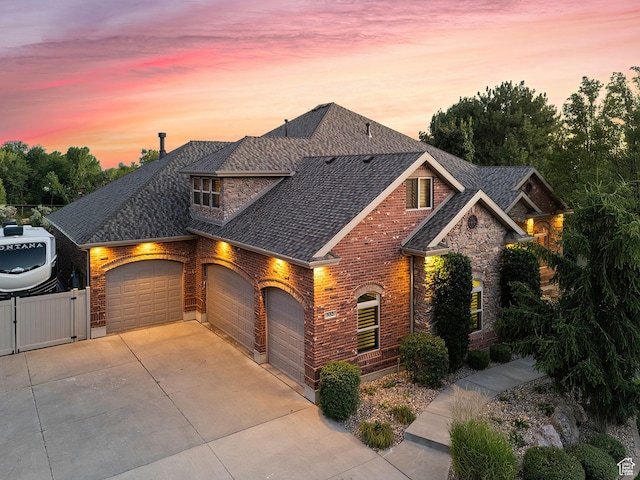 view of front of home featuring a gate, stone siding, concrete driveway, an attached garage, and brick siding