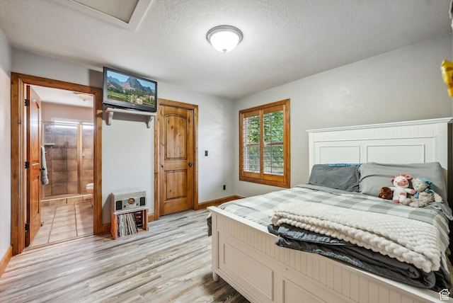 bedroom with a textured ceiling, baseboards, connected bathroom, attic access, and light wood-style floors