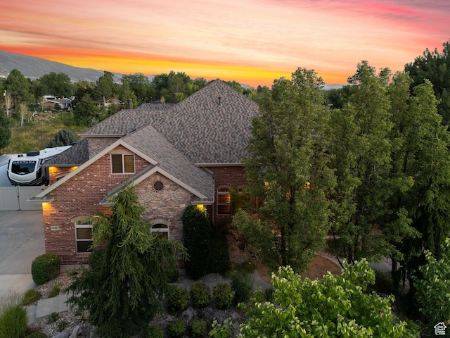 view of front of house with stone siding, roof with shingles, concrete driveway, brick siding, and a mountain view