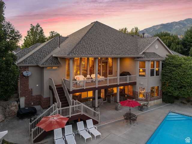 back of property at dusk with an outdoor pool, stucco siding, stairway, outdoor dining space, and a patio area