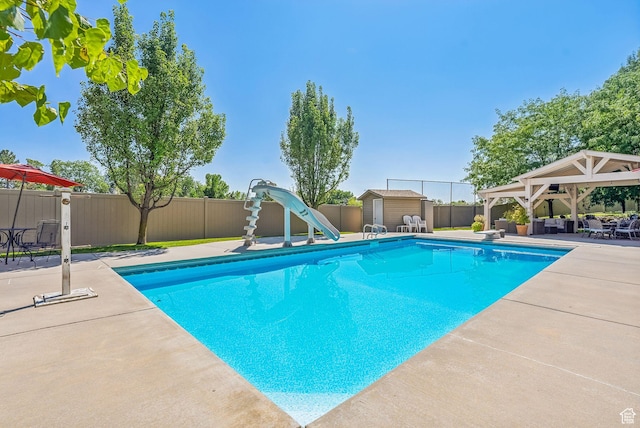 view of pool with a gazebo, a water slide, a storage shed, a fenced backyard, and a patio