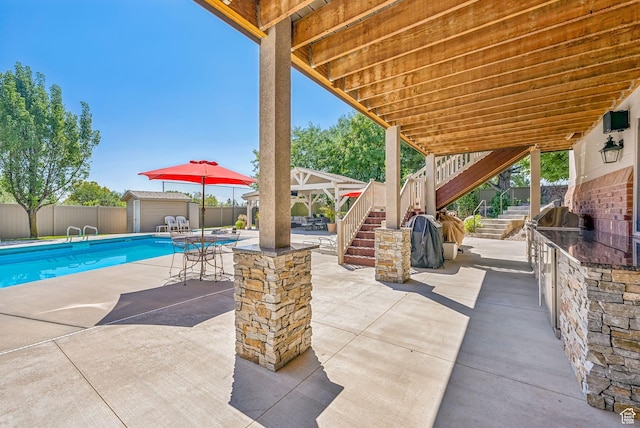 view of patio / terrace featuring stairs, an outdoor kitchen, a shed, an outbuilding, and a fenced backyard