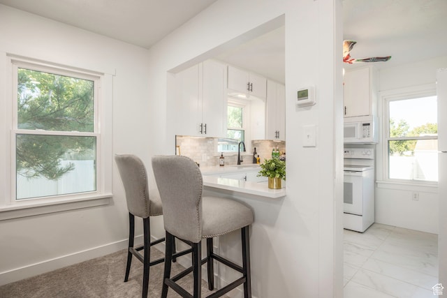 kitchen with white appliances, backsplash, light tile patterned floors, sink, and white cabinets