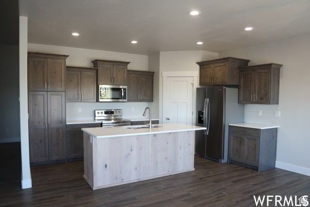 kitchen with stainless steel appliances, dark hardwood / wood-style floors, sink, and a kitchen island with sink