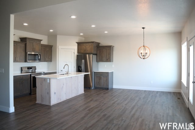 kitchen with an inviting chandelier, sink, dark hardwood / wood-style floors, appliances with stainless steel finishes, and a center island with sink