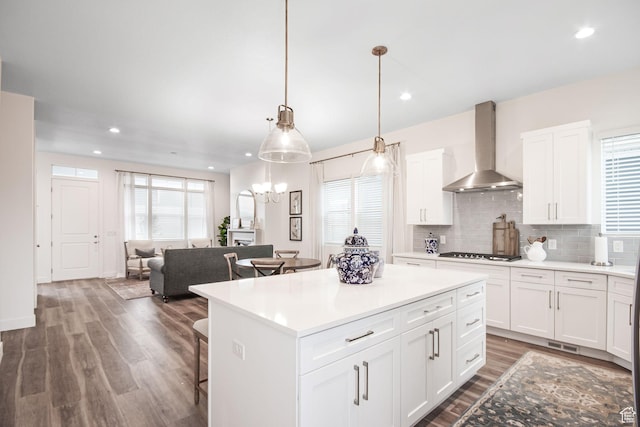 kitchen featuring stainless steel gas stovetop, wall chimney range hood, decorative backsplash, a kitchen breakfast bar, and wood finished floors