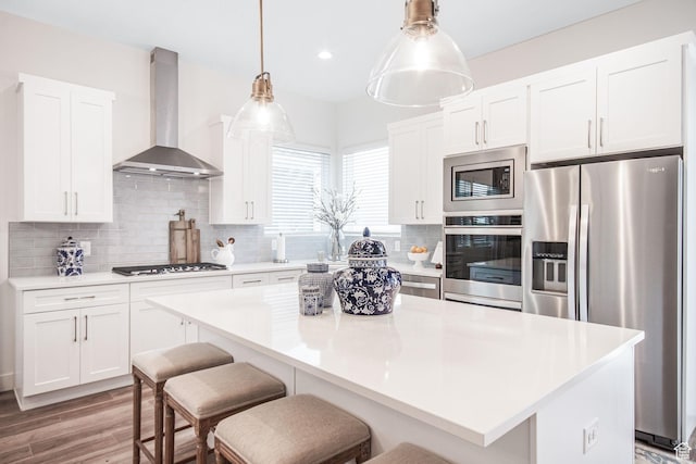 kitchen featuring tasteful backsplash, a center island, white cabinetry, stainless steel appliances, and wall chimney range hood