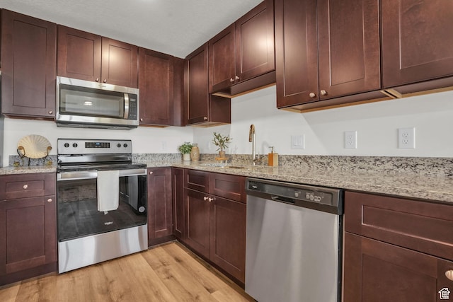 kitchen with a sink, light wood-style flooring, light stone countertops, and stainless steel appliances