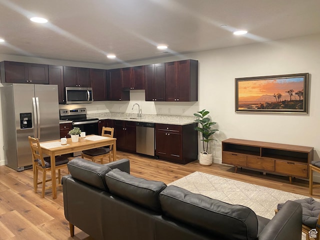 kitchen with light wood-type flooring, a sink, open floor plan, recessed lighting, and appliances with stainless steel finishes