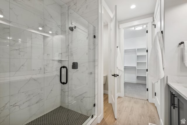 bathroom with a marble finish shower, a walk in closet, vanity, and wood finished floors