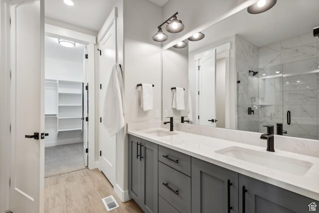 full bathroom featuring a marble finish shower, double vanity, a sink, and wood finished floors