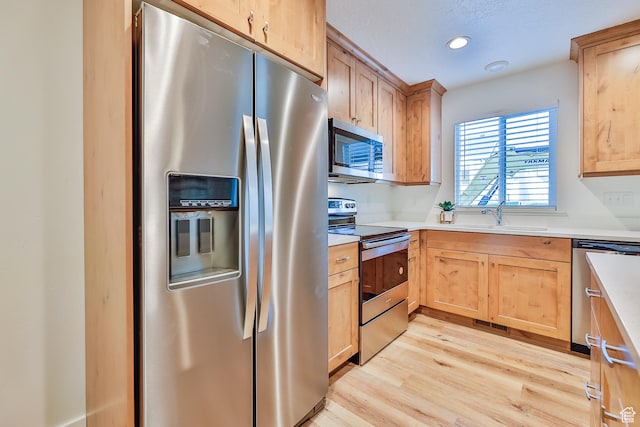kitchen featuring a sink, light wood-style flooring, appliances with stainless steel finishes, and light brown cabinetry