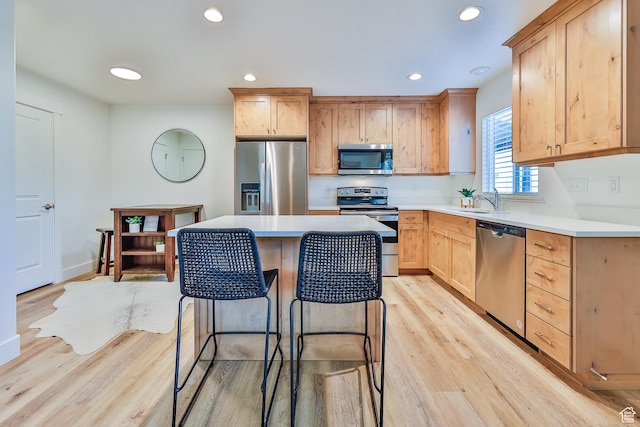 kitchen featuring appliances with stainless steel finishes, a breakfast bar, a sink, light wood-style floors, and recessed lighting