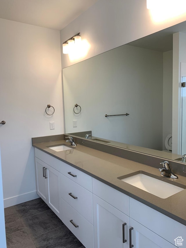 full bath with double vanity, a sink, toilet, and baseboards
