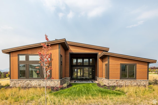 back of property with stone siding and a lawn