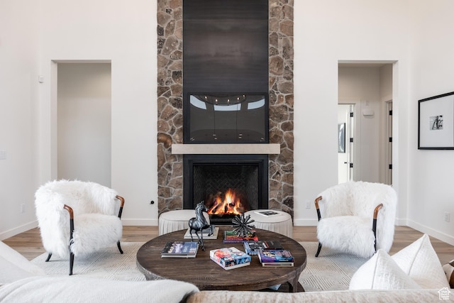 living room featuring a stone fireplace, baseboards, and wood finished floors